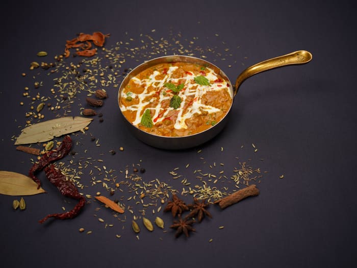Dal makhani in a copper pan surrounded by whole spices