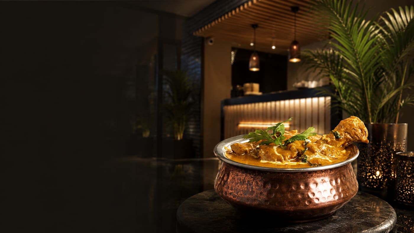A copper handi of butter chicken on a marble table in the dining room
