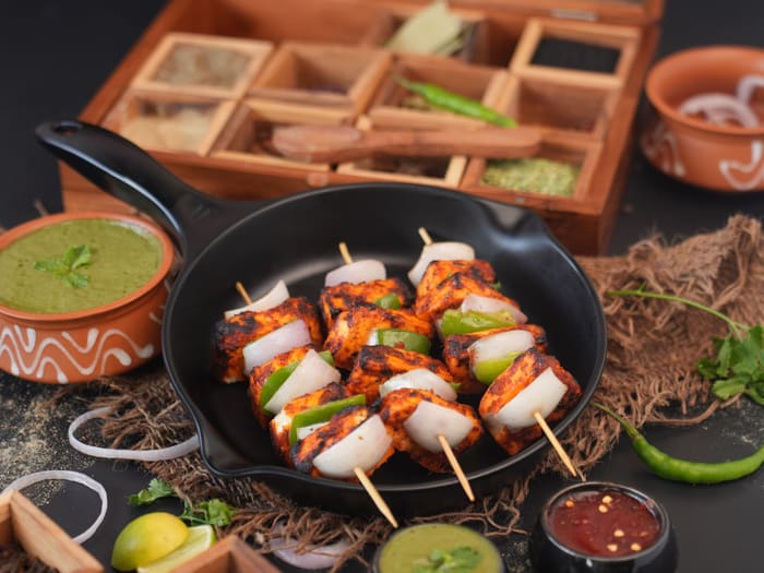Paneer tikka skewers grilled in a cast iron pan